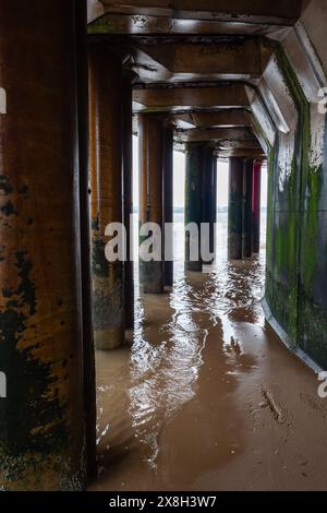 Rostige Metallsäulen unter dem Pier mit Wellen, die die Textur und die Auswirkungen der Natur auf künstliche Strukturen hervorheben Stockfoto