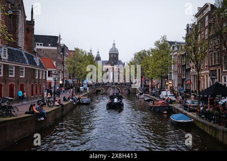 Niederlande, Amsterdam - 6. April 2024: Blick auf die Basilika des Heiligen Nikolaus und traditionelle alte Gebäude und Boote entlang eines Kanals Stockfoto