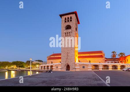 Evangelismos-Kirche in Rhodos, Griechenland in der Dämmerung. Beleuchteter Glockenturm und ruhiger Blick aufs Wasser Stockfoto