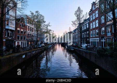 Niederlande, Amsterdam - 10. April 2024: Amsterdamer Grachtenhäuser, Fahrräder und Brücken in der Abenddämmerung im Stadtteil Jordaan Stockfoto