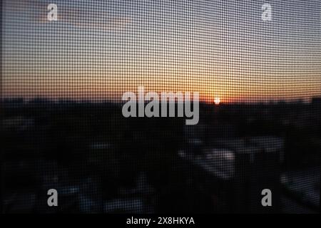 Sonnenuntergang durch einen Bildschirm - warme Orange- und Gelbtöne - Silhouette des fernen Horizonts. Aufgenommen in Toronto, Kanada. Stockfoto