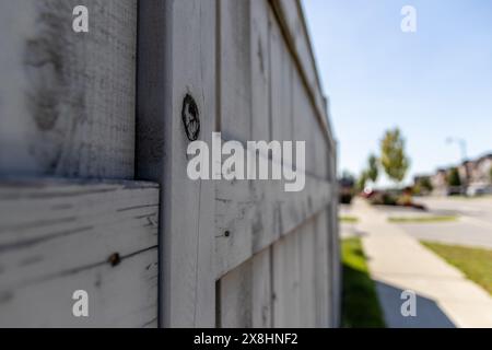 Nahaufnahme des verwitterten Holzzauns - Vorstadtgegend - Knoten in Holz und abblätternde weiße Farbe - klarer blauer Himmel. Aufgenommen in Toronto, CA Stockfoto