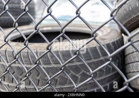 Gestapelte Altreifen – sichtbar durch einen Kettenzaun – konzentrieren sich auf Textur und Laufflächenmuster. Aufgenommen in Toronto, Kanada. Stockfoto