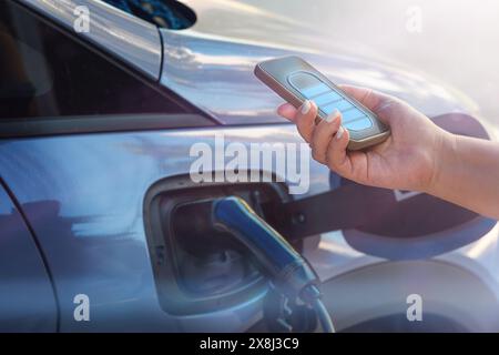 Frau Hand hält Handy EV für Auto im Freien Stockfoto