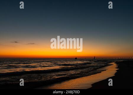 Ein goldener Horizont wird zum tiefblauen Himmel, wenn die Sonne über dem Lake Michigan in Grand Haven, Michigan, untergeht Stockfoto