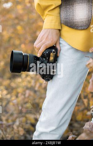 Nahaufnahme einer professionellen Fotokamera. Eine junge Dame steht im Herbstwald. Stockfoto