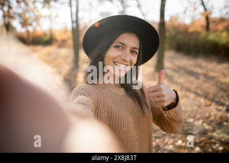Porträt einer hispanischen Frau vor Laub im Herbstpark, die Selfie macht. Stockfoto