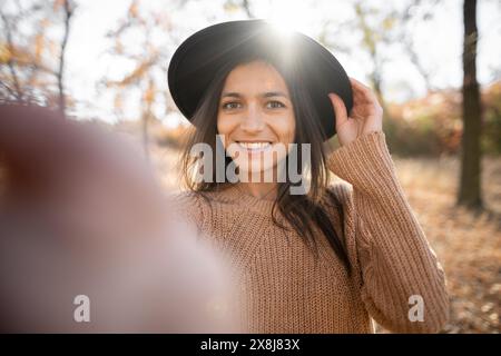 Porträt einer hispanischen Frau vor Laub im Herbstpark, die Selfie macht Stockfoto