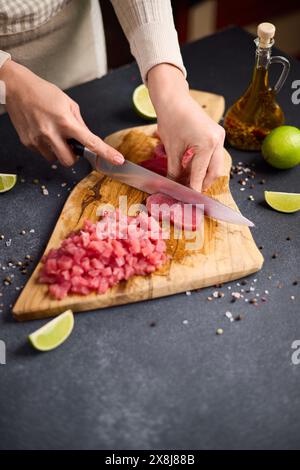 Frau Schnitt Thunfischsteak in Scheiben auf einem hölzernen Schneidebrett in der Hausküche Stockfoto