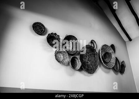 Zehn Korbkörbe in verschiedenen Farben hängen an einer weißen Wand, Schwarzweiß-Fotografie von Strohkörben Stockfoto