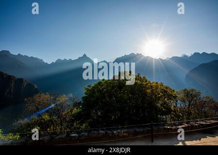 Sonnenaufgang zwischen Bäumen und Inkaruinen mit den Berggipfeln der Anden im Hintergrund in der östlichen Kordillera im Süden Perus Stockfoto