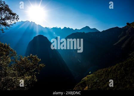 Sonnenaufgang zwischen Bäumen und Inkaruinen mit den Berggipfeln der Anden im Hintergrund in der östlichen Kordillera im Süden Perus Stockfoto