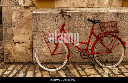 Altes, rotes Fahrrad, das an die Wand gelehnt ist, mit einem Platten Reifen auf dem Fahrrad Stockfoto