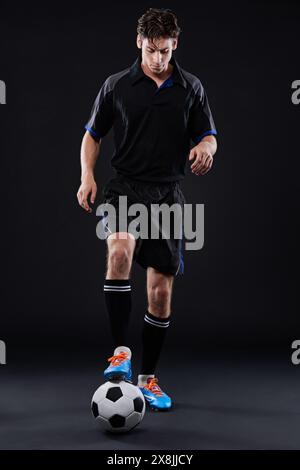 Fitness, Geschick und Fußball mit Mann im Studio für Freizeitsporttraining isoliert auf schwarzem Hintergrund. Freestyle, Kontrolle und junger Mann Stockfoto