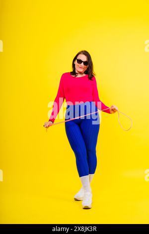 Hübsch lächelnde, pralle Frau in sportlichem Oberteil und Leggings, die ein Springseil in den Händen hält Stockfoto
