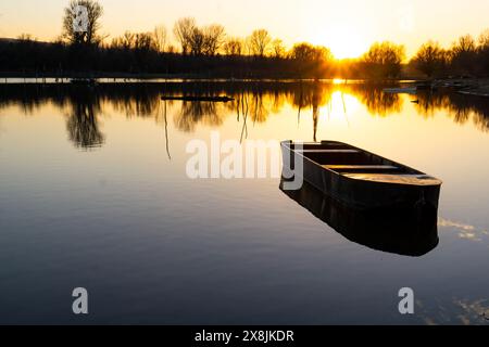 Ruhiges Boot schwimmt bei Sonnenuntergang auf ruhigem Wasser, umgeben von Silhouettenbäumen auf der Donauinsel Sodros in der Nähe von Novi Sad, Serbien Stockfoto