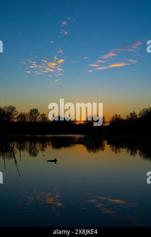 Ein ruhiger Sonnenuntergang färbt den Himmel in warmen Farbtönen, die sich perfekt im ruhigen Wasser spiegeln, während der Tag in die Nacht auf der Donauinsel Sodros in der Nähe von Novi Sad übergeht Stockfoto