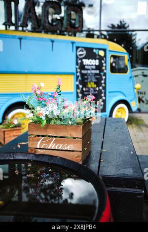 Manchester UK . Stadtleben, Blumen in Holzkiste auf rustikalem Cafétisch von blau-gelben Taco-Truck, schaffen lebendige Street Food Szene. Stockfoto