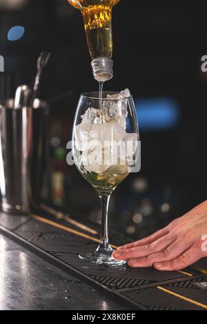 Nahaufnahme eines Barkepers, der eine goldene Flüssigkeit in ein Glas mit Eiswürfeln an einer Bar gießt Stockfoto