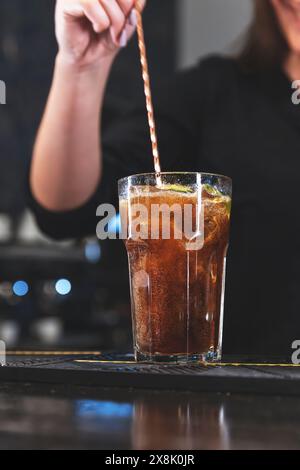 Nahaufnahme einer Hand, die in einem modernen Café ein erfrischendes Glas Eiskaffee rührt Stockfoto