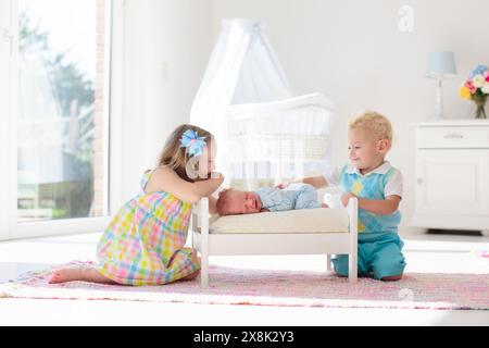 Lustiges, glückliches Kleinkind, das mit neugeborenem Jungen im Spielzeugbett spielt. Kinder spielen zu Hause. Weißes Kinderzimmer für Bruder und Schwester. Kind im sonnigen Schlafzimmer. Stockfoto