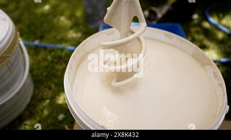 Mischen von Farbe in einem Eimer. Er mischt draußen weiße Farbe in einem Eimer. Mischen Sie Farbe in einem Eimer, um die Außenseite des Hauses zu streichen. Stockfoto