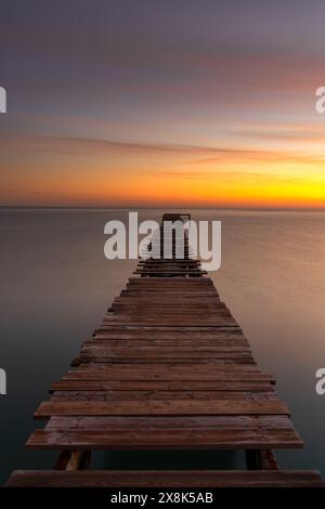 Friedliche Meereslandschaft bei Sonnenaufgang mit einem alten hölzernen Dock, der in das ruhige Meer führt Stockfoto