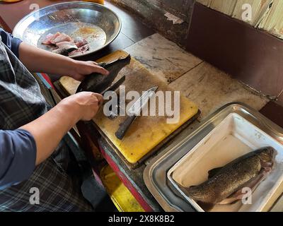 Der Koch schneidet Forellenfisch auf einem Holzbrett in der Küche. Fisch zum Kochen vorbereiten. Stockfoto