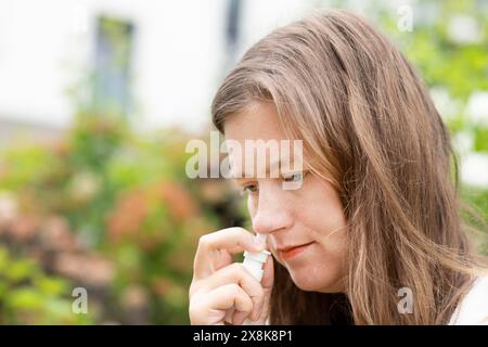 Junge Frau leidet an Heuschnupfen und sprüht sich draußen die Nase, Freiburg, Baden-Württemberg, Deutschland Stockfoto