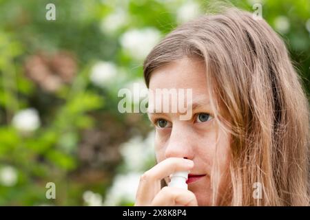 Junge Frau leidet an Heuschnupfen und sprüht sich draußen die Nase, Freiburg, Baden-Württemberg, Deutschland Stockfoto