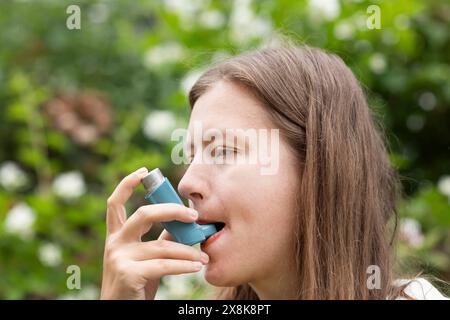 Junge Frau leidet an Heuschnupfen und inhaliert Asthmaspray im Freien, Freiburg, Baden-Württemberg, Deutschland Stockfoto