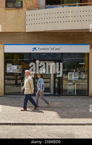 Viladecans, Barcelona, Spanien-26. Mai 2024: Bild der Fassade eines Büros der La Caixa Foundation mit zwei Personen, die auf dem Bürgersteig spazieren. Ideal für iact Stockfoto