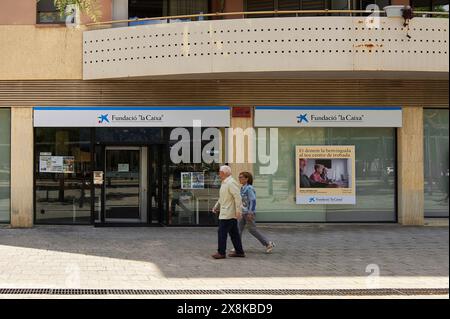 Viladecans, Barcelona, Spanien-26. Mai 2024: Bild der Fassade eines Büros der La Caixa Foundation mit zwei Personen, die auf dem Bürgersteig spazieren. Stockfoto