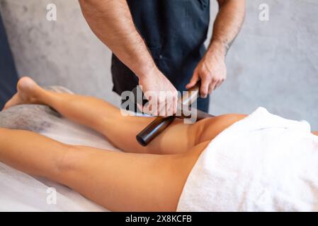 Kreolische Massage mit Bambusstäben an den Füßen einer Frau in einem Spa-Salon. Lymphdrainagesamassage der Schienbeinmuskulatur. Stockfoto