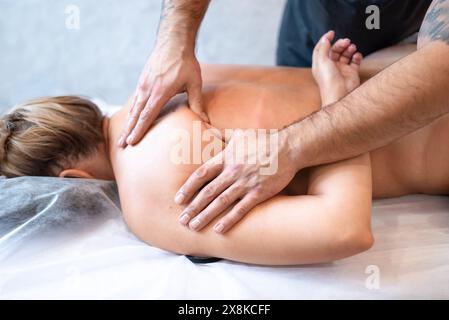 Der männliche Masseur massiert die Rücken- und Schulterblätter der Frau, die auf einem Massagetisch auf hellem Hintergrund liegt. Das Konzept der Massagebehandlungen. Stockfoto