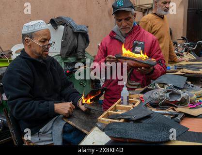 Marrakesch, Marokko - 23. März 2024: Traditionelle Schuhmacher im Souk der Medina von Marrakesch kleben neue Sohlen auf alte Schuhe Stockfoto