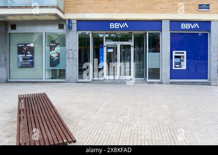 Viladecans, Barcelona, Spanien-26. Mai 2024: BBVA-Bankfiliale auf einem städtischen Bürgersteig. Das Bild zeigt den Haupteingang aus Glas, einen Geldautomaten und eine Holzbank Stockfoto