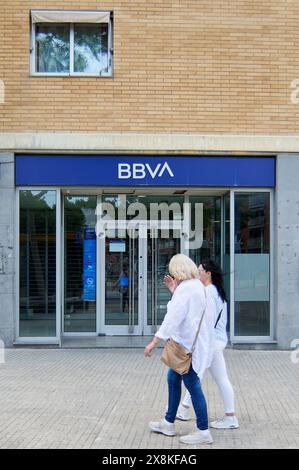 Viladecans, Barcelona, Spanien-26. Mai 2024: Bild des Haupteingangs einer BBVA-Filiale mit Glastüren und Geldautomat. Zwei Frauen gehen an Th vorbei Stockfoto