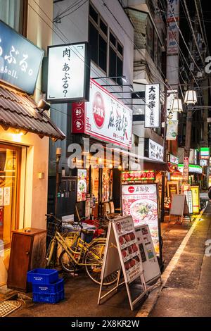 Eine Reihe japanischer Restaurants entlang einer Straße in Otsuka, Tokio, am Abend. Verschiedene Menütafeln auf der Zahlung und Neonschilder über den Eingängen. Stockfoto