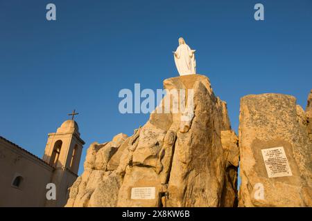 Calvi, Haute-Corse, Korsika, Frankreich. Imposante Statue der Jungfrau Maria auf felsigem Felsvorsprung an der Chapelle Notre Dame de la Serra, Sonnenaufgang. Stockfoto