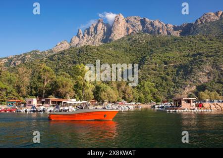 Porto, Corse-du-Sud, Korsika, Frankreich. Abendlicher Blick über den Fluss Porto zu den hohen Granitklippen von Capo d'Orto, vorbei an einem roten Motorkreuzer. Stockfoto