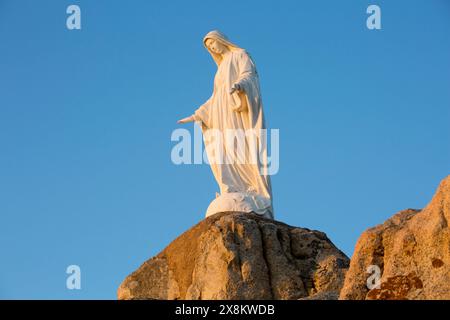 Calvi, Haute-Corse, Korsika, Frankreich. Imposante Statue der Jungfrau Maria auf felsigem Felsvorsprung an der Chapelle Notre Dame de la Serra, Sonnenaufgang. Stockfoto