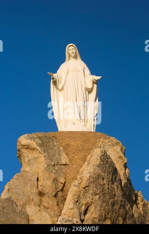 Calvi, Haute-Corse, Korsika, Frankreich. Imposante Statue der Jungfrau Maria auf felsigem Felsvorsprung an der Chapelle Notre Dame de la Serra, Sonnenaufgang. Stockfoto