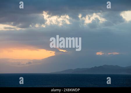 L’Ile-Rousse, Haute-Corse, Korsika, Frankreich. Rosafarbene Wellen der frühen Morgensonne, die durch dunkle Wolken über dem Désert des Agriates scheint. Stockfoto