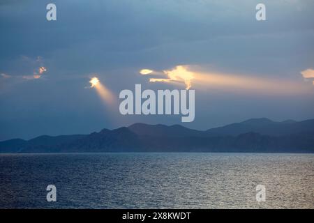 L’Ile-Rousse, Haute-Corse, Korsika, Frankreich. Rosafarbene Wellen der frühen Morgensonne, die durch dunkle Wolken über dem Désert des Agriates scheint. Stockfoto