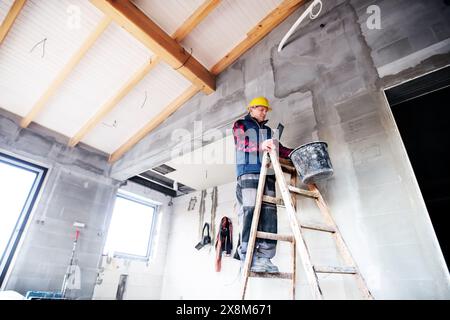 Bauarbeiter, der auf einer Leiter steht und an der Wand arbeitet. Stockfoto