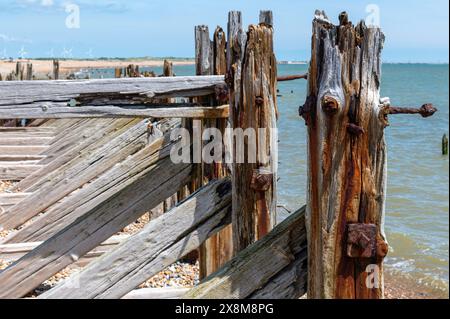 Abgenutzter, groyne Pfostenkopf, stark verwittertes Holz, rostige Bolzen und Rostflecken im Rye Harbour Nature Reserve an hellen, sonnigen Tagen. Windturbinen am Horizont Stockfoto