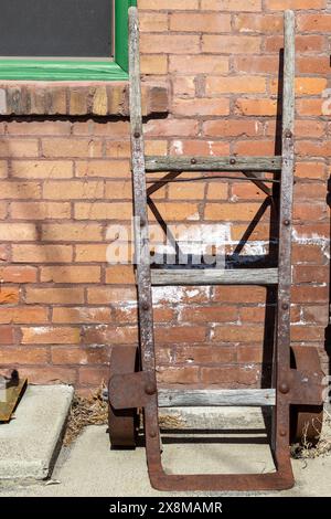 Alte, hölzerne, rostfreie Metallkarre, die auf einer Ziegelwand ruht Stockfoto