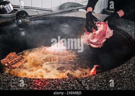 In der Küche eines Restaurants in Usbekistan in Taschkent kocht der männliche Koch Lammfleisch in einem Kessel für traditionelles orientalisches usbekisches Pilaw Stockfoto