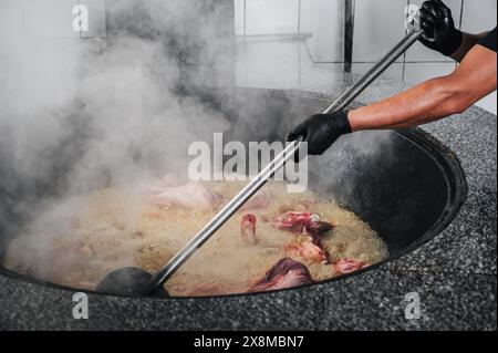 In der Küche des Restaurants in Usbekistan in Taschkent kocht der männliche Koch Fleisch im kochenden Kessel für das traditionelle orientalische usbekische Pilaw Stockfoto
